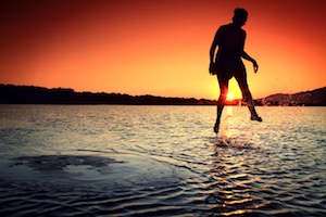 a man jumping into the water at sunset.