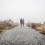 two people walking down a dirt road in the fog.