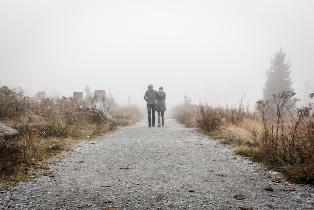 two people walking down a dirt road in the fog.