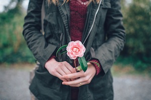 a woman holding a pink rose in her hands.