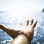 a person's hand reaching out towards the water.