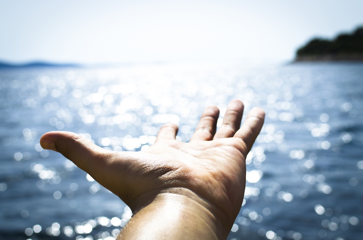a person's hand reaching out towards the water.