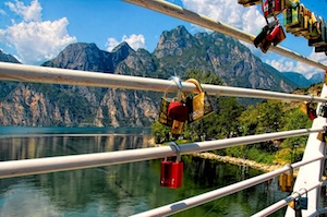 padlocks on a railing near a lake with mountains in the background.
