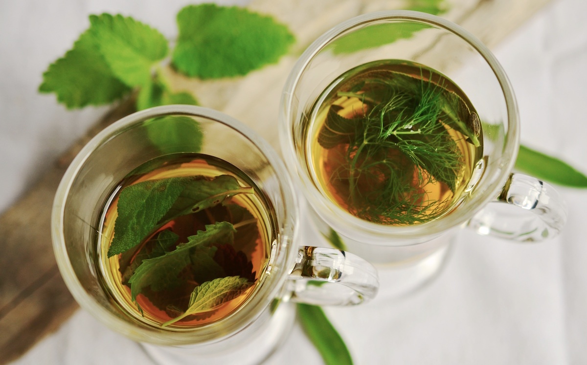 two glasses of tea with green leaves in them.