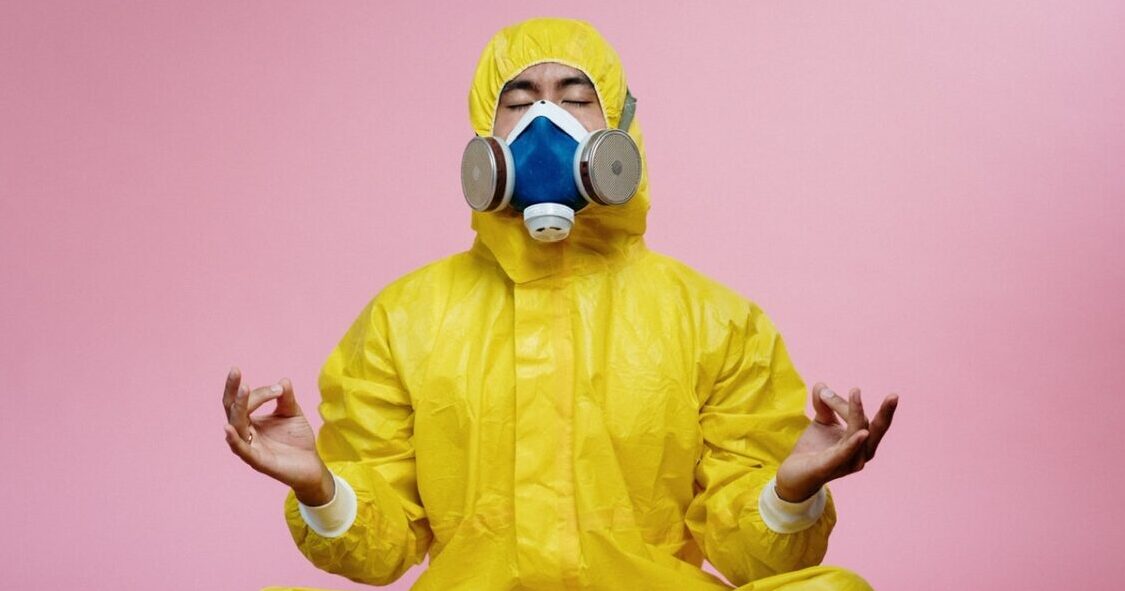 a man in a yellow suit and gas mask sitting in a yoga pose.
