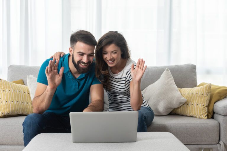 a man and woman sitting on a couch looking at a laptop.