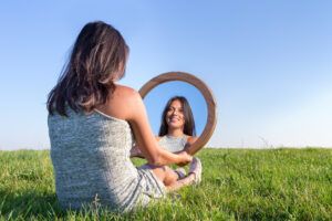 a woman sitting in the grass holding a circular mirror.