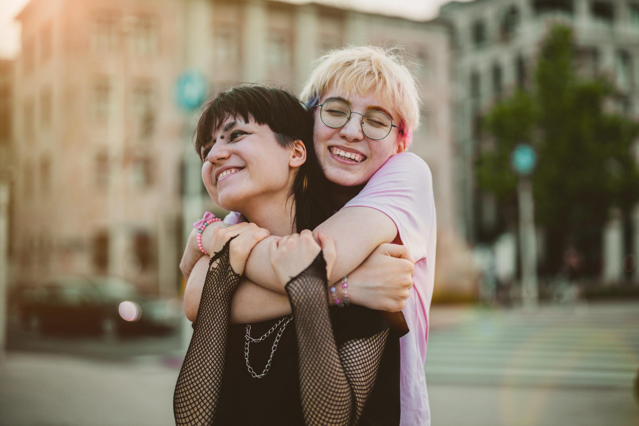 two women hugging each other on a city street.