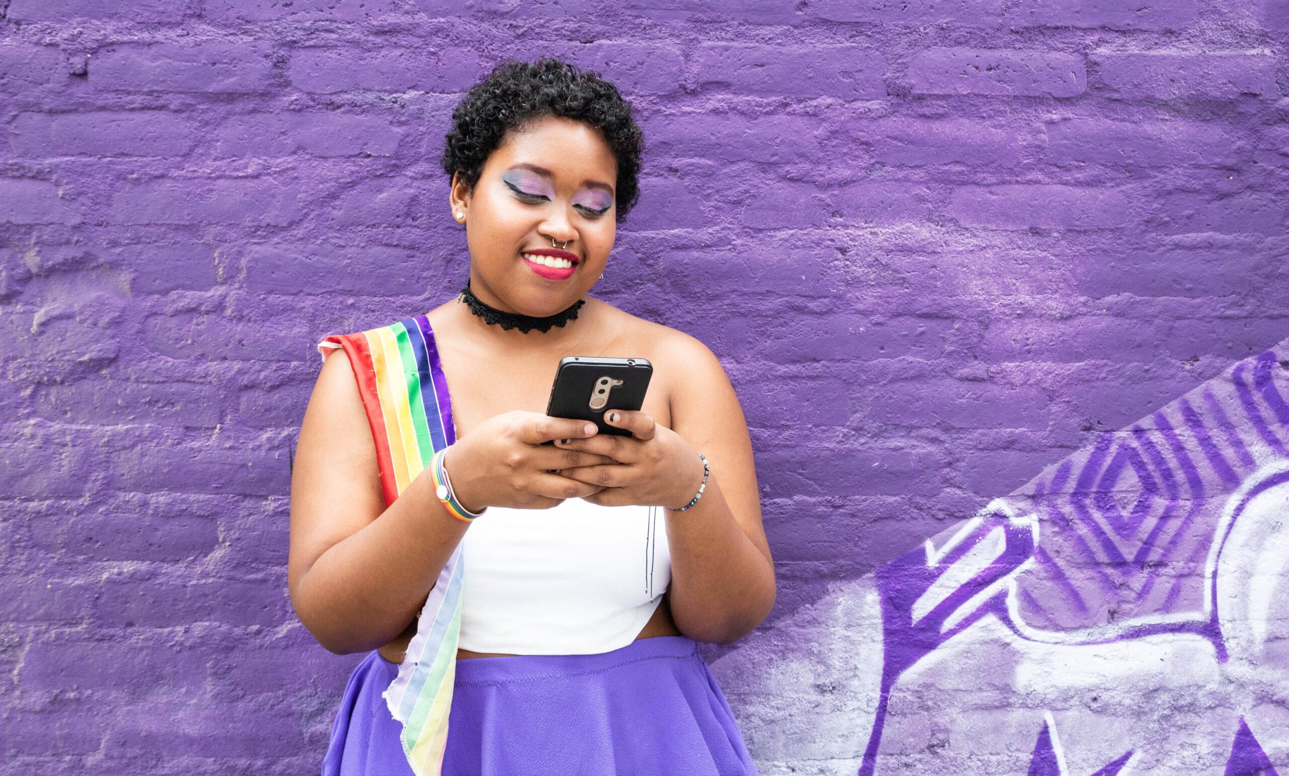 a woman standing in front of a purple wall looking at her cell phone.