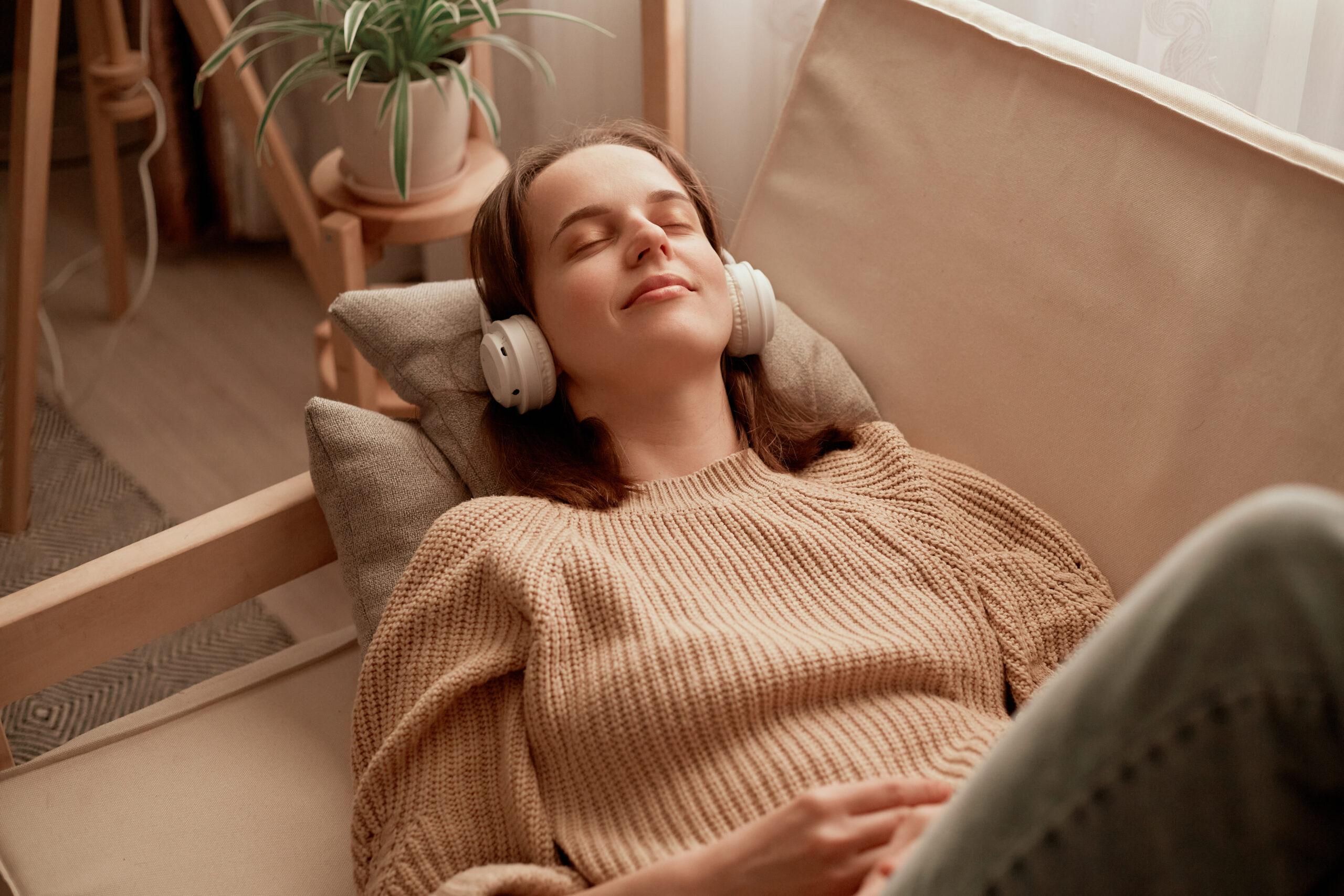 a woman laying on a couch listening to headphones.